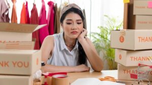 Seorang pemilik UMKM terlihat khawatir di tengah tumpukan kotak, menggambarkan kesalahan yang harus dihindari dalam bisnis digital.